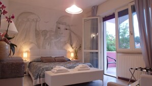 A bedroom with a large bed, a bedside table, a lamp, a vase with flowers, and a mural on the wall. - Hotel Julia (Comacchio)