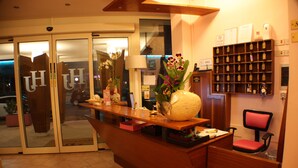 A reception desk with a vase of flowers, a lamp, and a chair. There is a wall-mounted shelf with keys and a sign above it. - Hotel Julia (Comacchio)