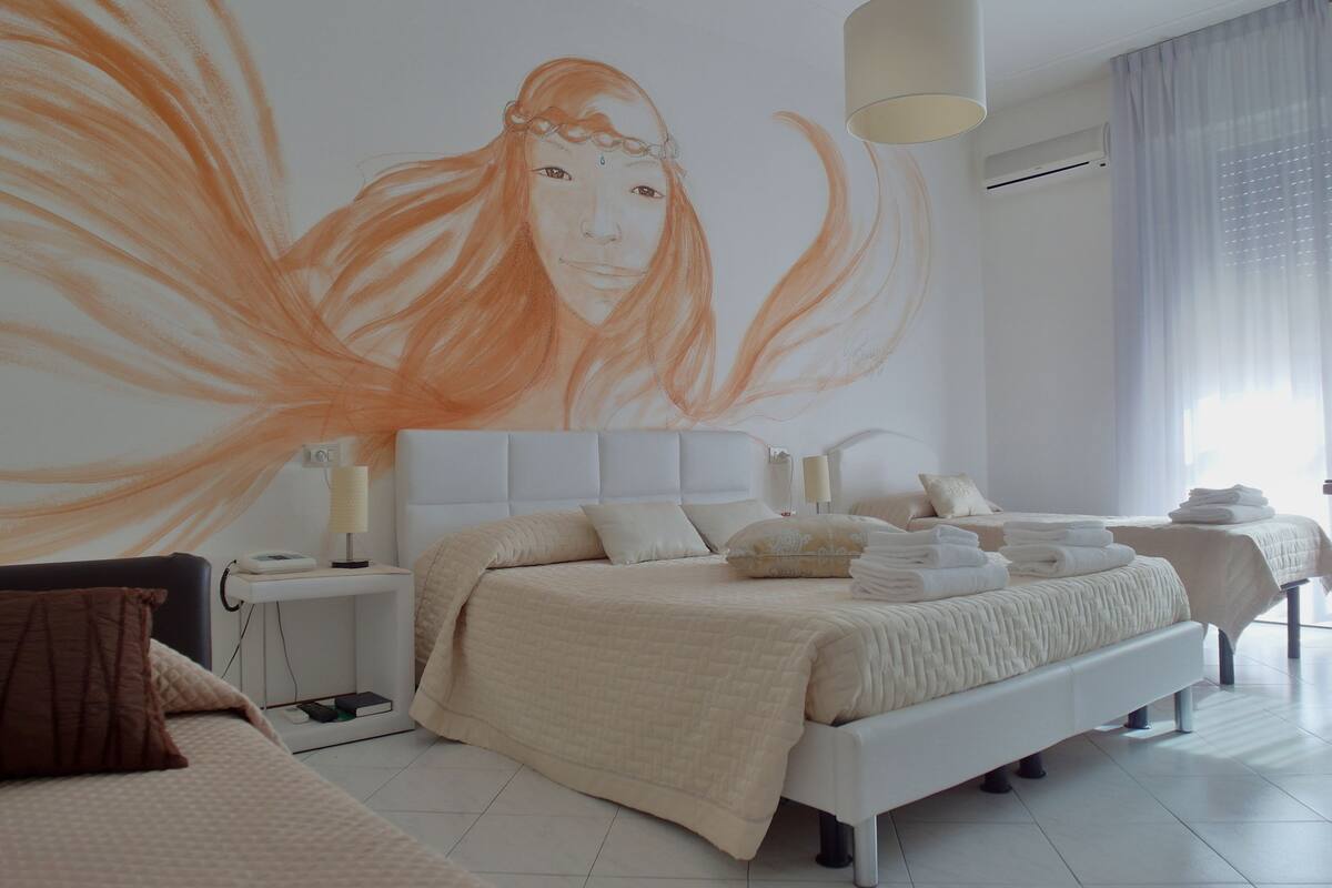 A modern hotel room with a large bed, a bedside table, a lamp, and a wall mural.