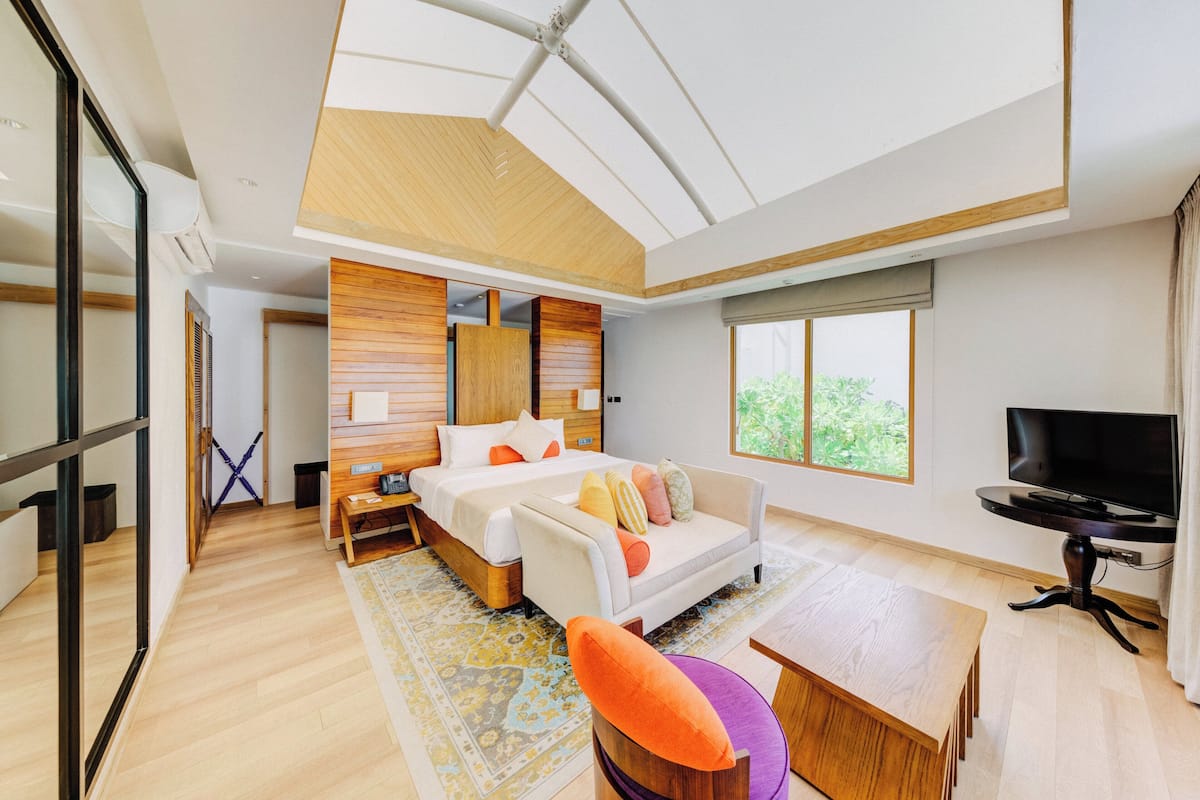 A modern bedroom with a large bed, a TV, and a view of greenery outside.