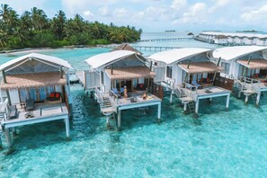 Overwater bungalows with thatched roofs, wooden walkways, and clear turquoise water. - Cinnamon Hakuraa Huraa Maldives - All Inclusive Adults-Only (Hakuraa Huraa)