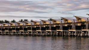 A row of overwater bungalows with thatched roofs, connected by walkways over water. - Cinnamon Hakuraa Huraa Maldives - All Inclusive Adults-Only (Hakuraa Huraa)