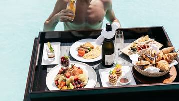 A dining table with a variety of food and drinks, including a bottle of wine, placed on a poolside deck.