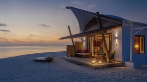 A beachfront villa with a curved roof, a deck, and a seating area with cushions and a table. - Cinnamon Hakuraa Huraa Maldives - All Inclusive Adults-Only (Hakuraa Huraa)