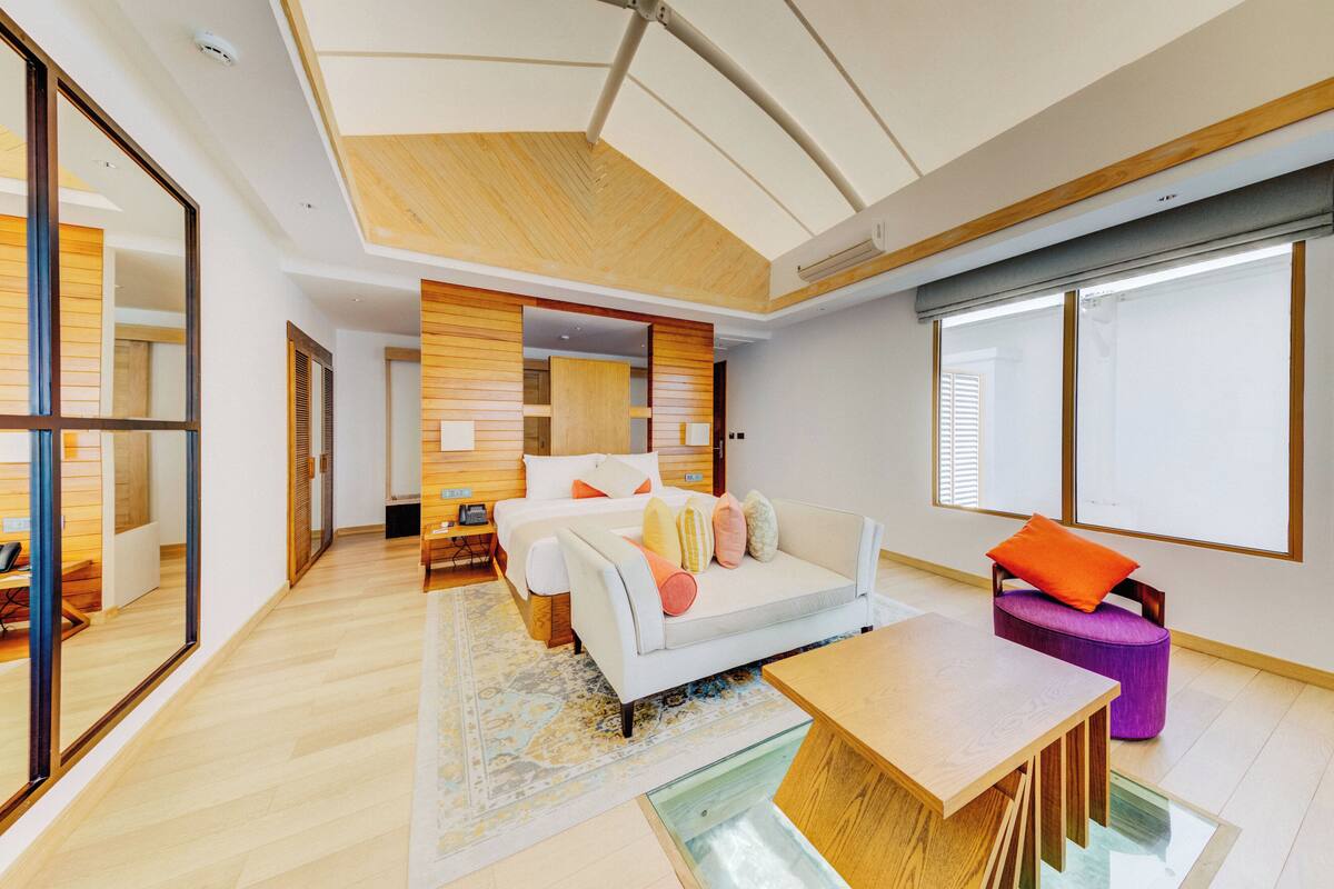 A modern hotel room with a large bed, a dining table, and a seating area.