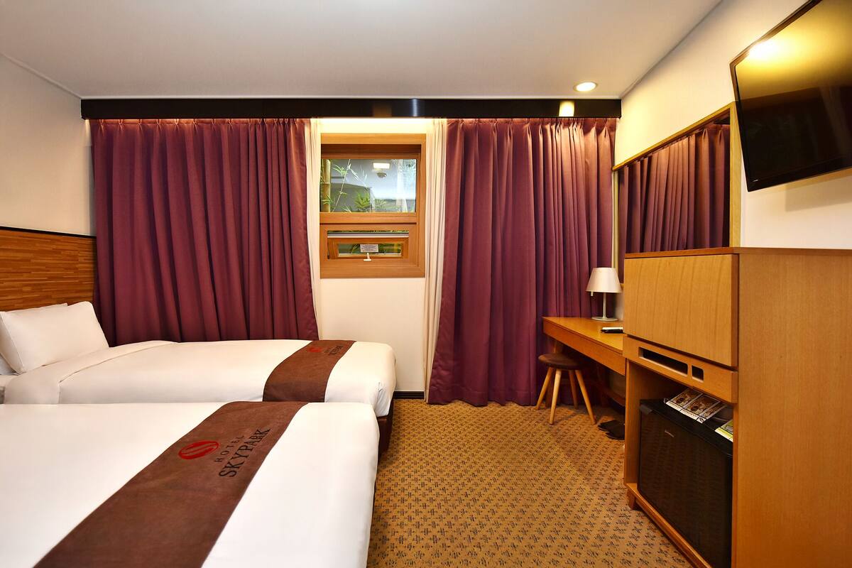 Habitación de hotel con dos camas, un escritorio, un televisor y una ventana con cortinas.