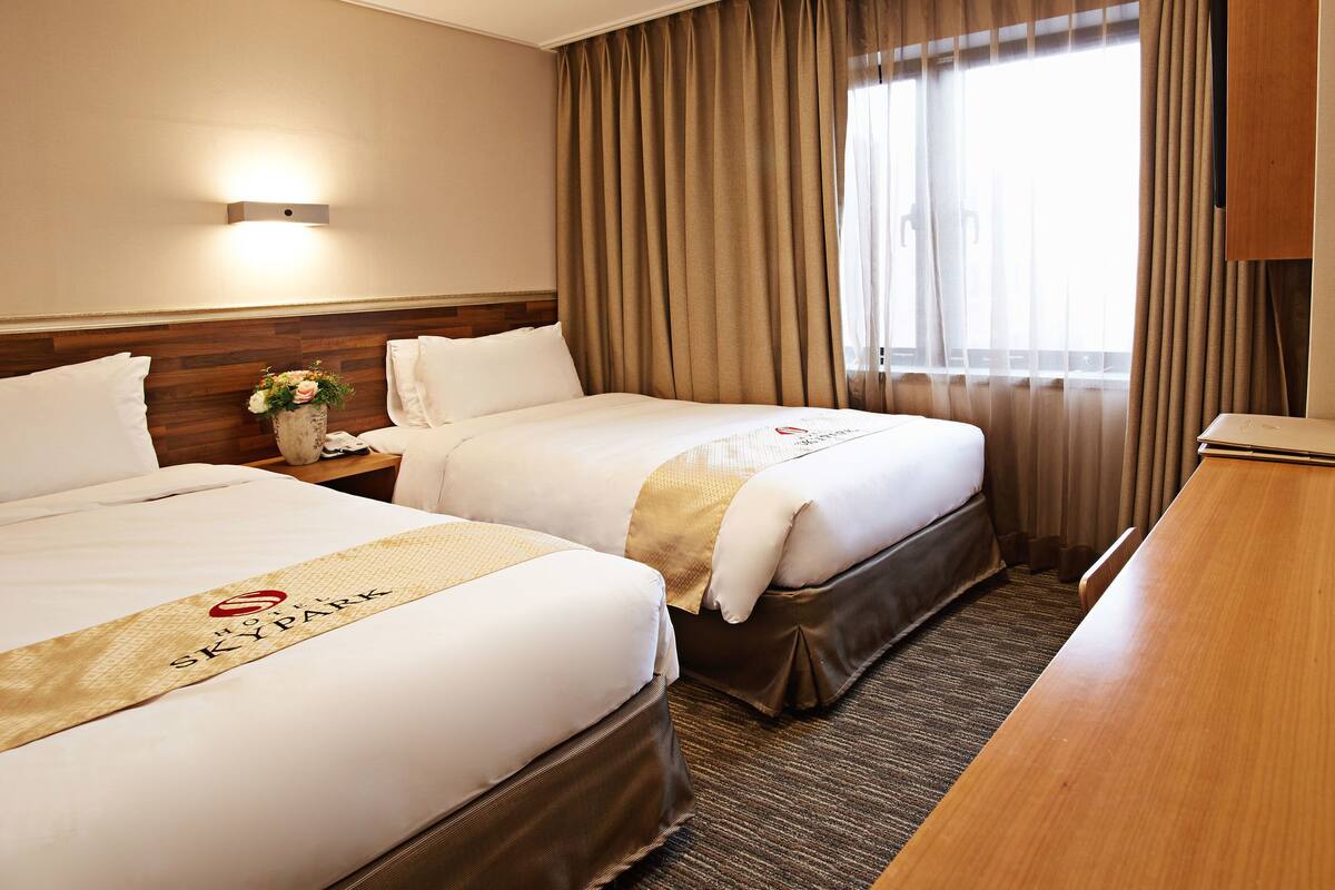 Habitación de hotel con dos camas, un escritorio de madera, una computadora portátil y un florero con flores.