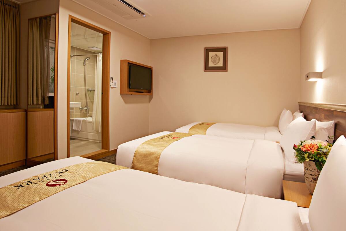 Una habitación de hotel con dos camas, baño y cabecera de madera.