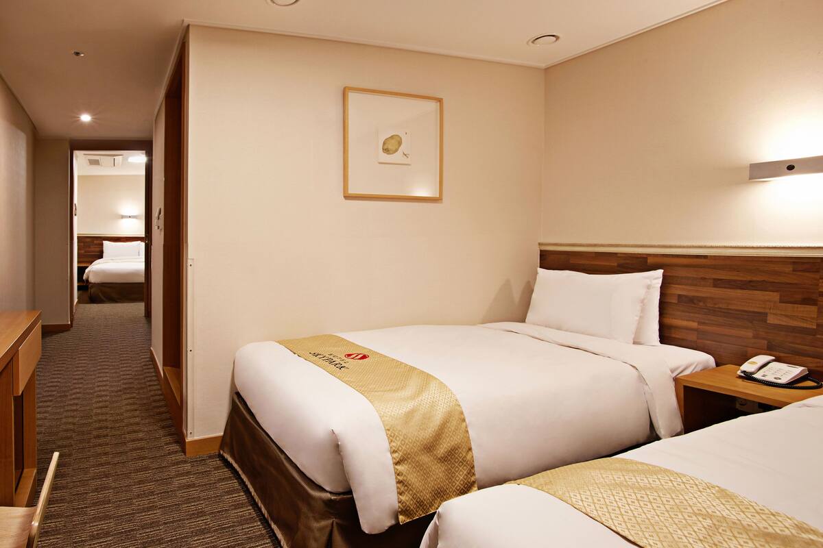Habitación de hotel con dos camas, cabecero de madera, mesita de noche con teléfono y un cuadro en la pared.