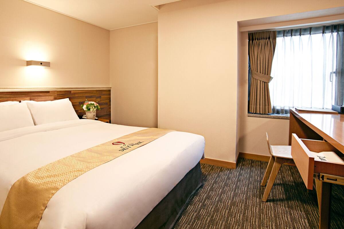 Una habitación de hotel con una cama grande, un escritorio y una ventana con cortinas.