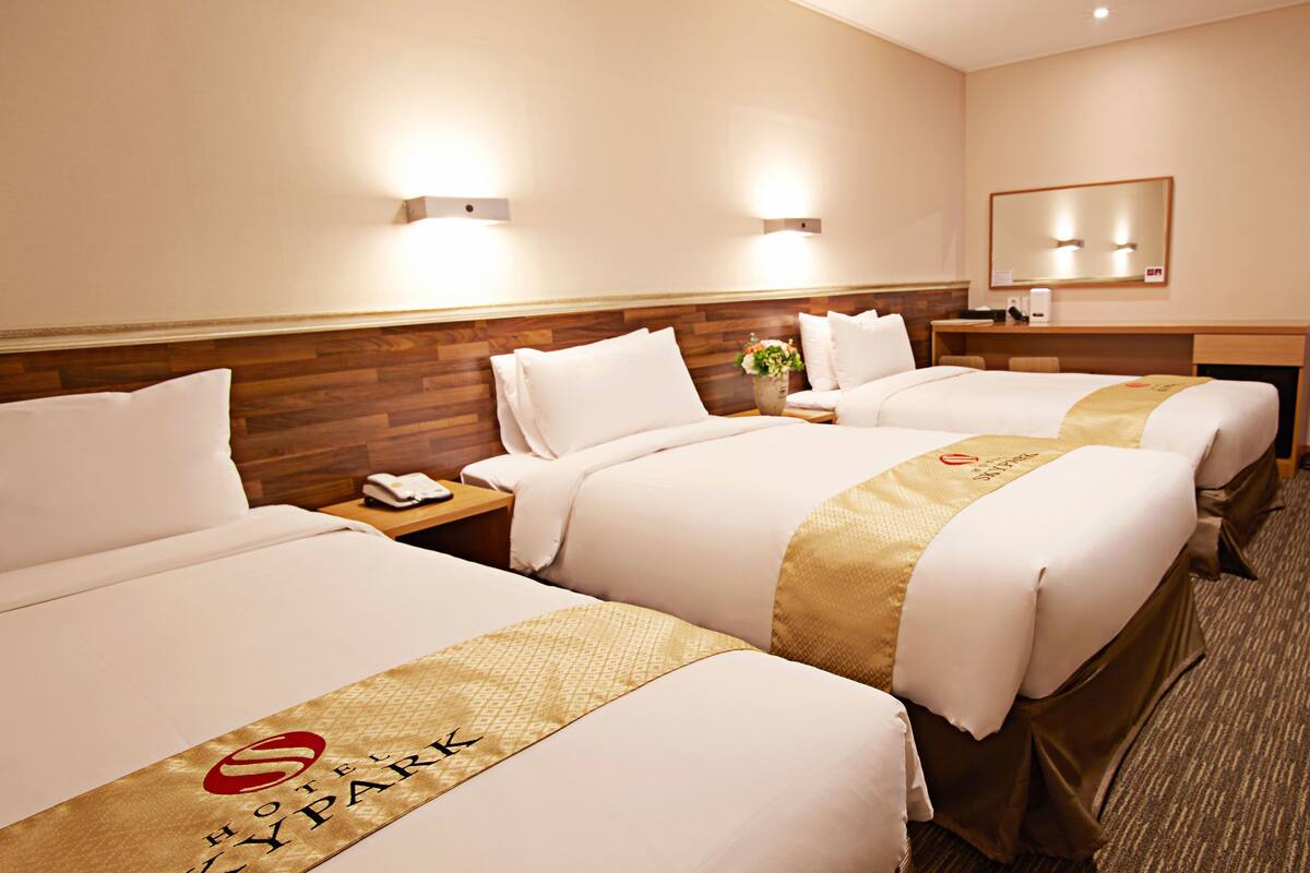 Una habitación de hotel con dos camas, un escritorio, un espejo y una mesita de noche con un teléfono.