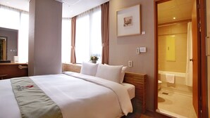 Una habitación de hotel con una cama, un escritorio, un teléfono y un baño visible a través de una puerta abierta.