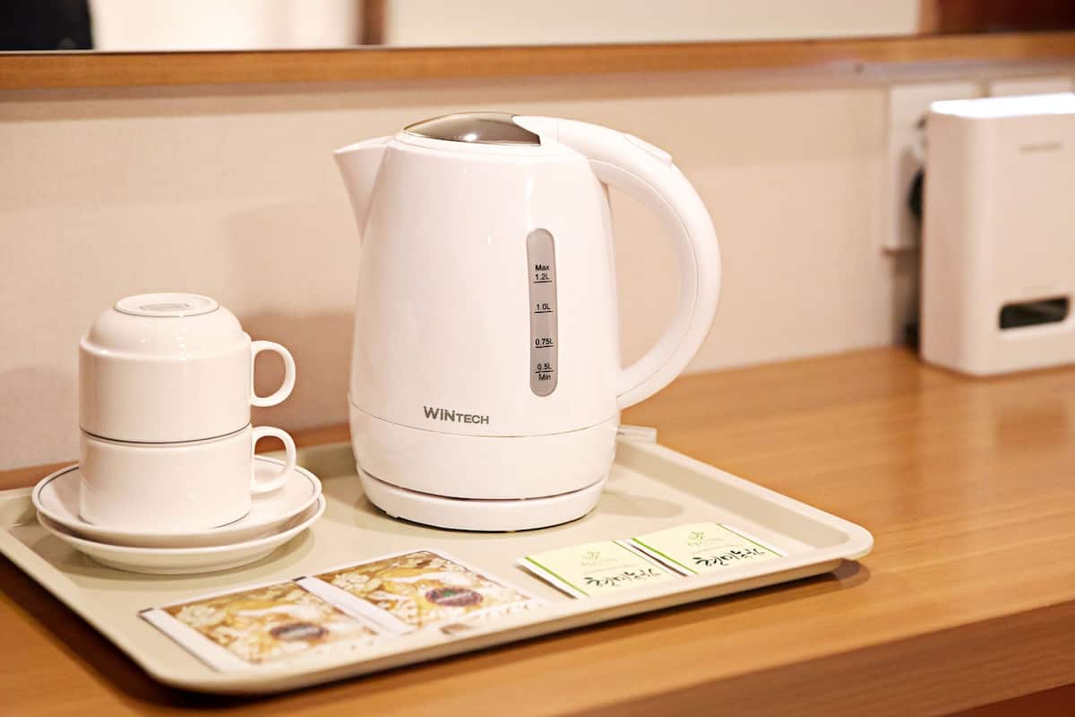 Una tetera eléctrica blanca con una bandeja, una taza y un platillo sobre una mesa de madera.
