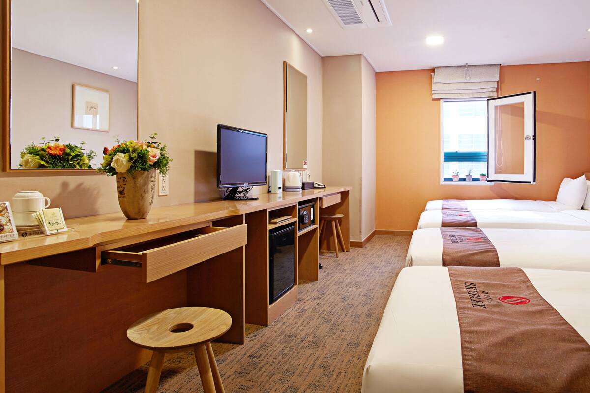 A hotel room with a desk, TV, and two beds.