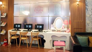 Een receptiebalie met drie computerschermen waarop '9 59' staat, een spiegel en een wastafel met cosmetica.