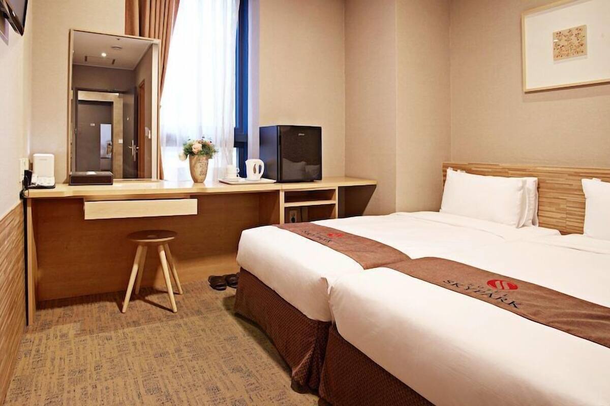 A hotel room with a bed, a desk with a computer, a chair, a mirror, and a window with curtains.