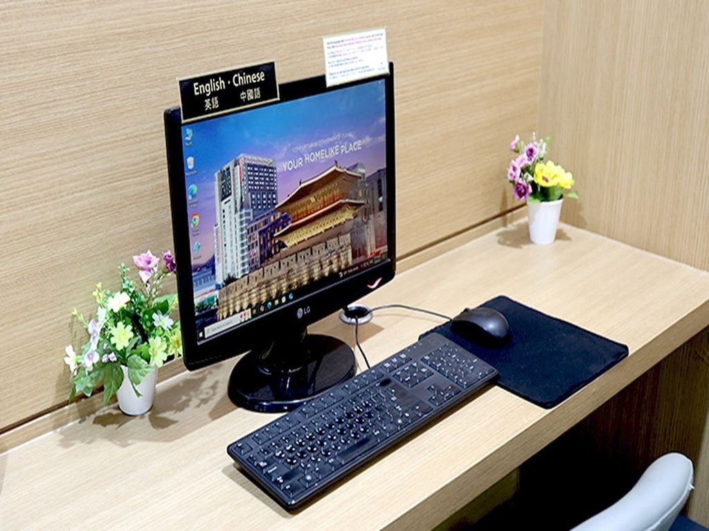 A computer monitor with a dual language display, a keyboard, a mouse, a desk, and a small potted plant.