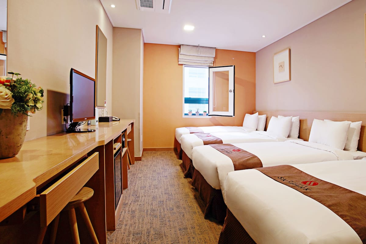 A hotel room with two beds, a desk, a computer, and a window with a view.