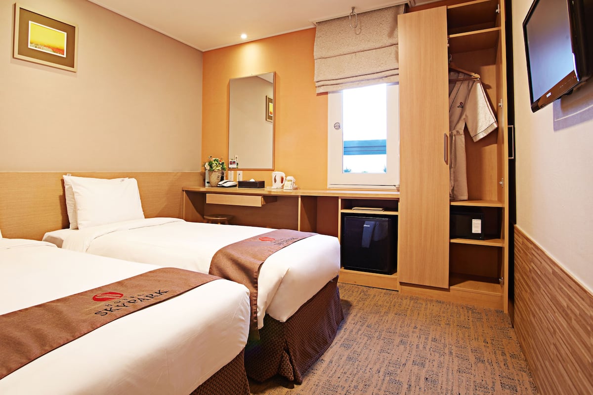 A hotel room with two beds, a desk with a mirror, a small seating area, and a wardrobe.