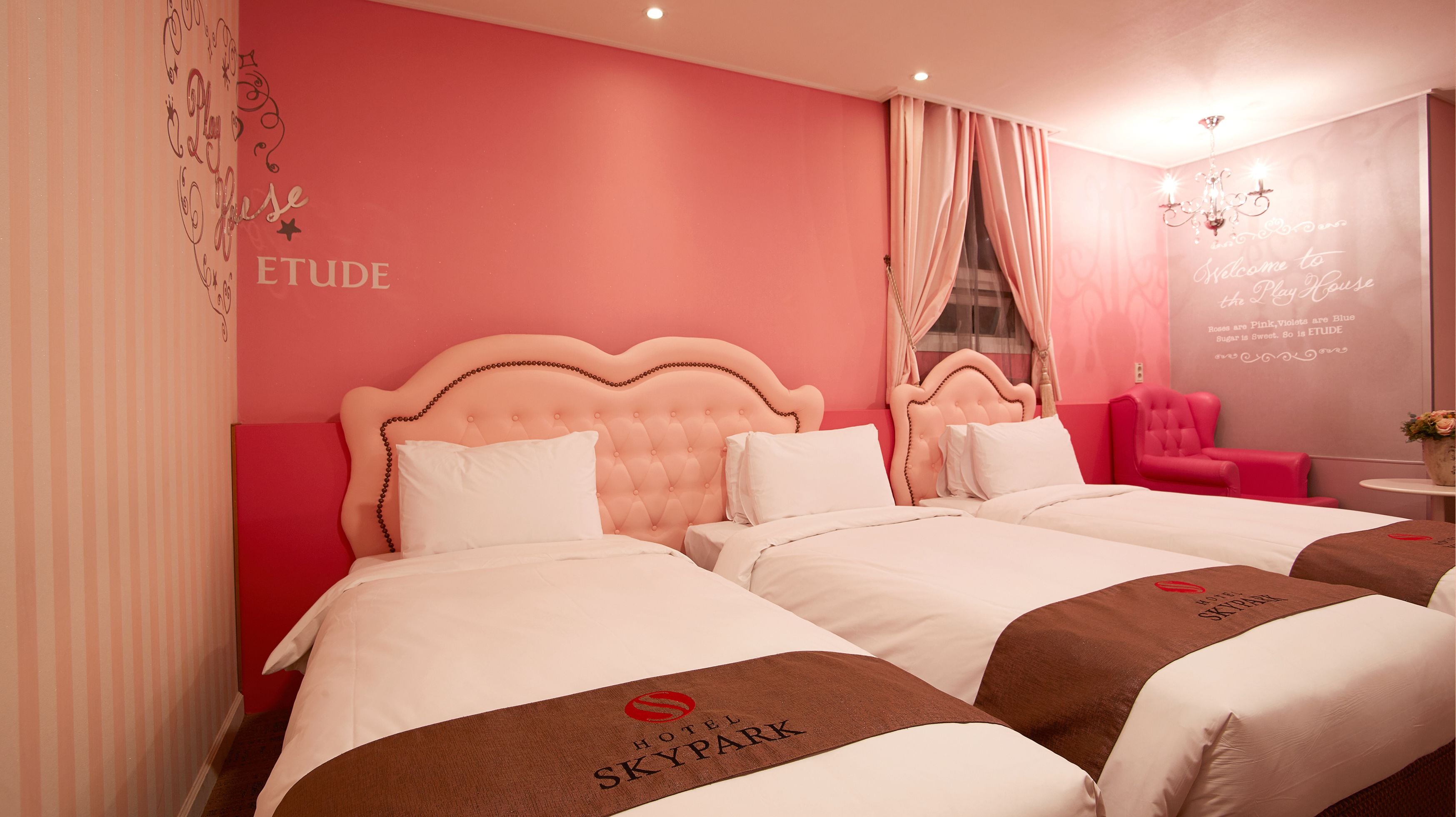 Habitación de hotel con dos camas, paredes rosadas y una silla roja.
