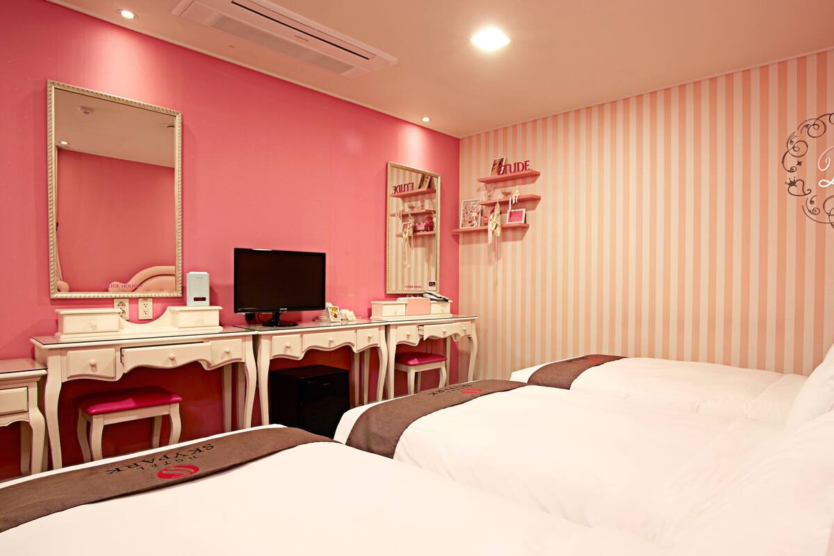 A pink-themed bedroom with a vanity, a bed, and a striped wall.