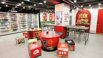 A food court with various food stalls, seating areas, and a beverage refrigerator.
