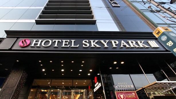 De ingang van Hotel Skypark III, met een modern ontwerp, met een opvallend bord en een reeks lampen boven de ingang.