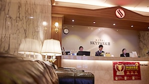 Ein Hotelrezeptionstresen mit drei Mitarbeitern, einer Uhr und einem Schild für Hotel SKYPARKIII.