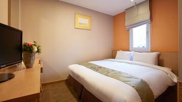 Een hotelkamer met een bed, een televisie op een bureau, een raam met uitzicht, en een ingelijste foto aan de muur.