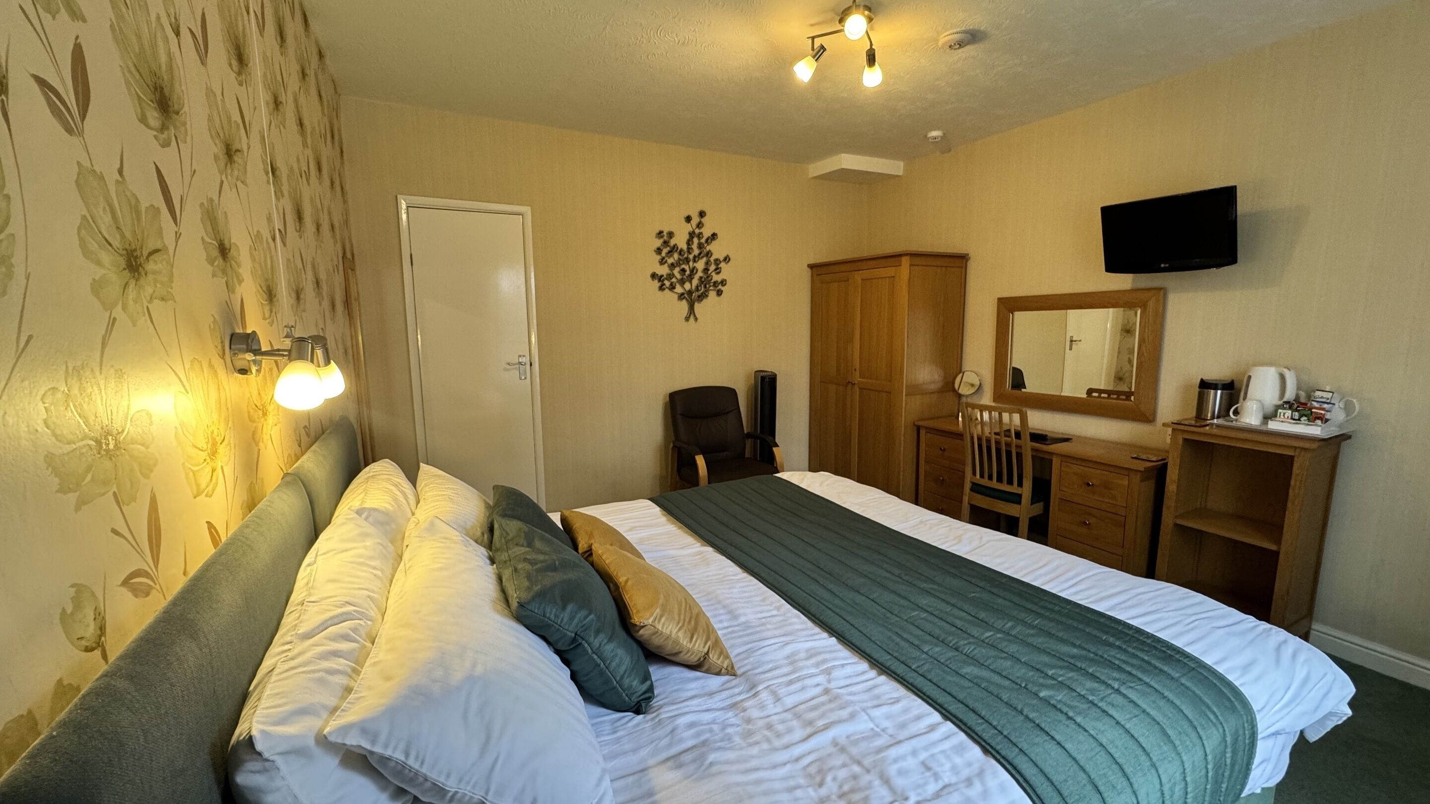 A hotel room with a bed, a desk, a chair, a television, and a door.