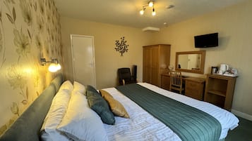 A hotel room with a bed, a desk, a chair, a television, and a door.