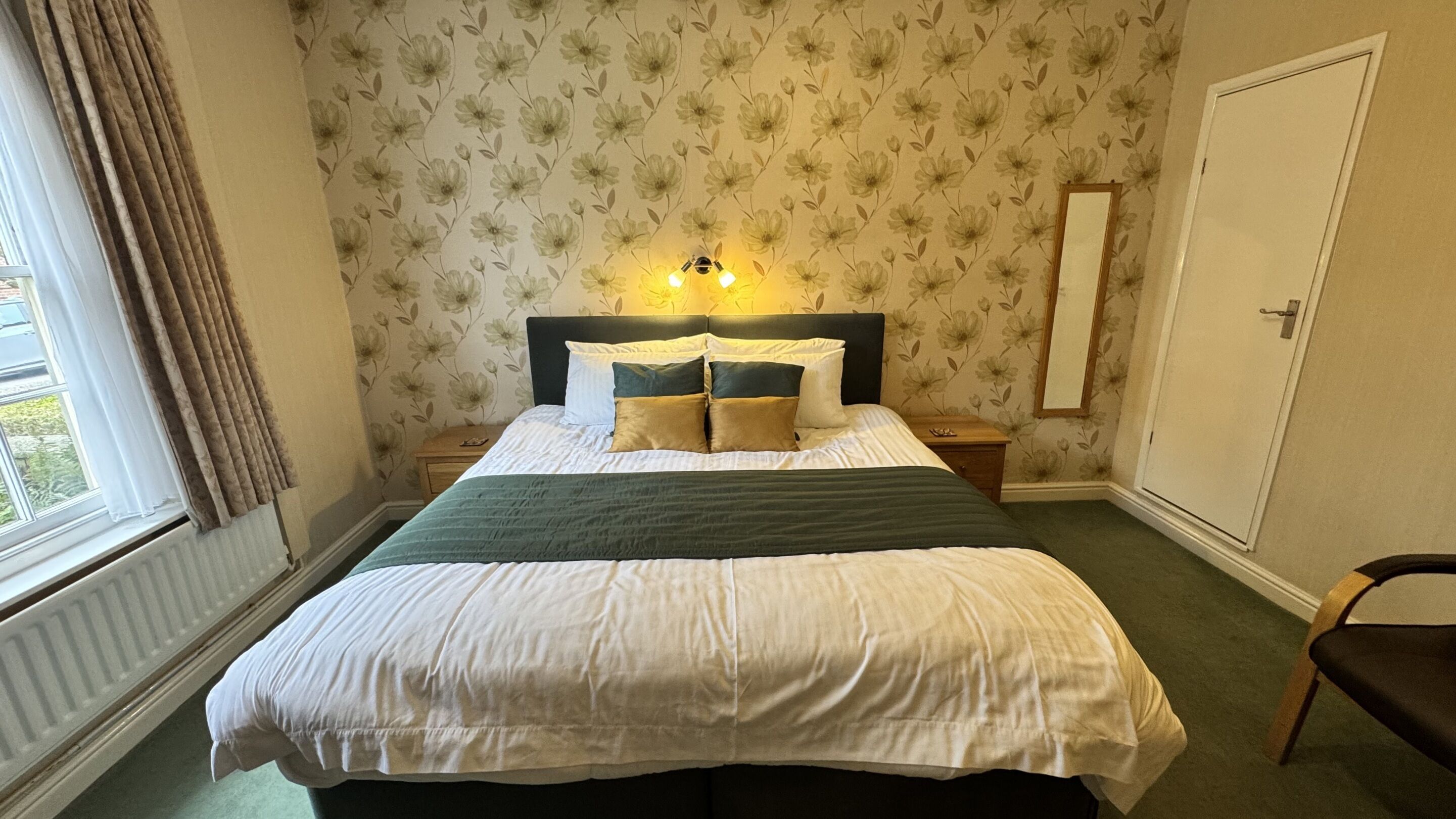 A bedroom with a bed, nightstands, a mirror, and a window with curtains.