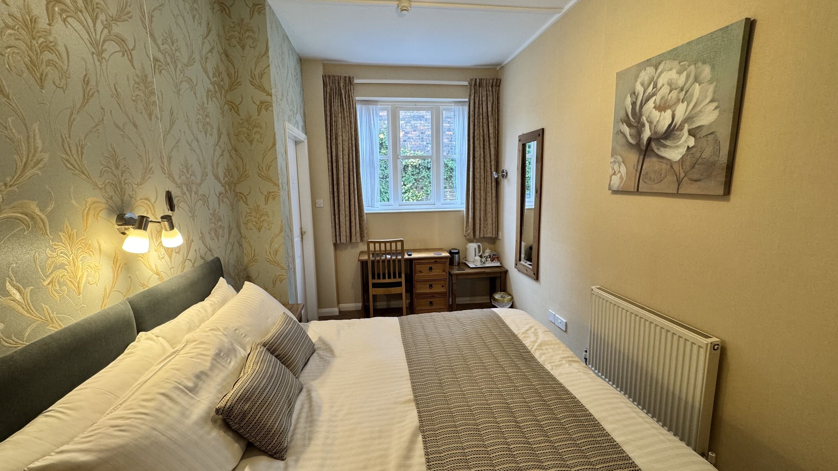 A bedroom with a bed, a desk, a chair, a radiator, and a window with curtains.
