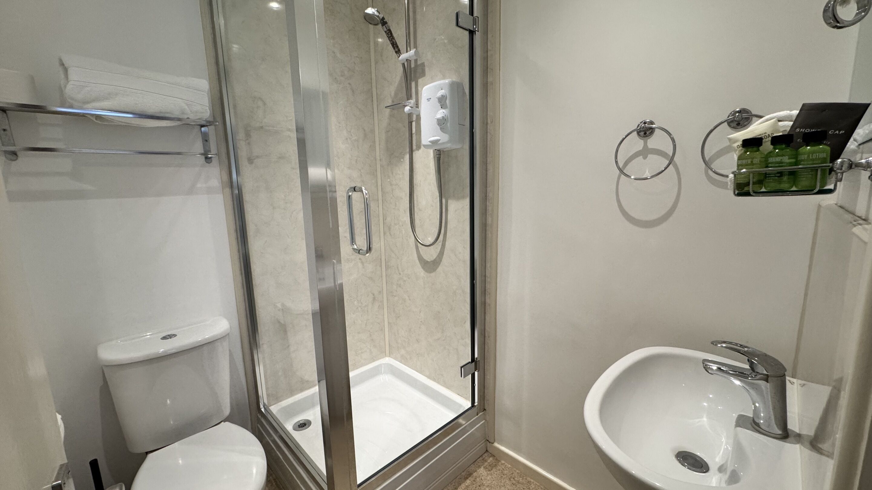 A modern bathroom with a glass-enclosed shower, a toilet, a sink with a mirror, and toiletries on a shelf.