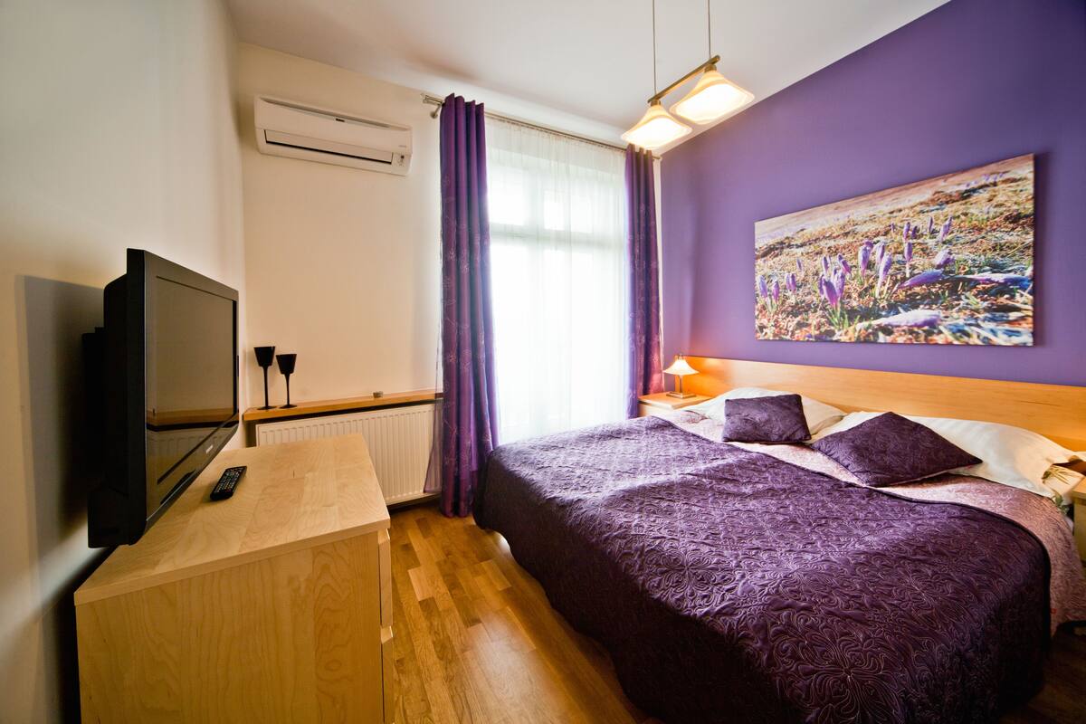 A hotel room with a bed, a TV, a wooden desk, and a painting on the wall.
