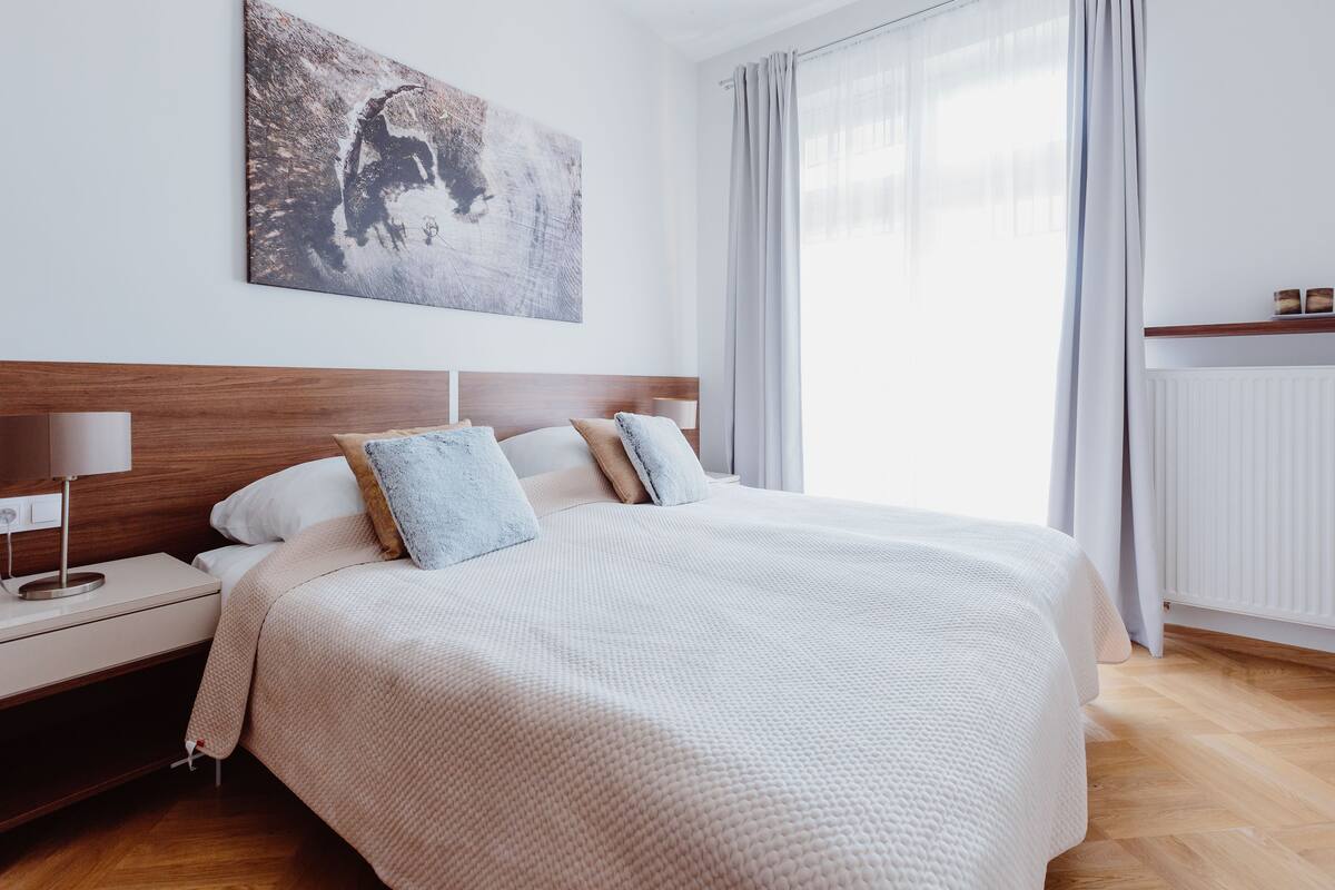 A neatly arranged bedroom with a large bed, a nightstand, a bedside lamp, and a wall-mounted artwork.
