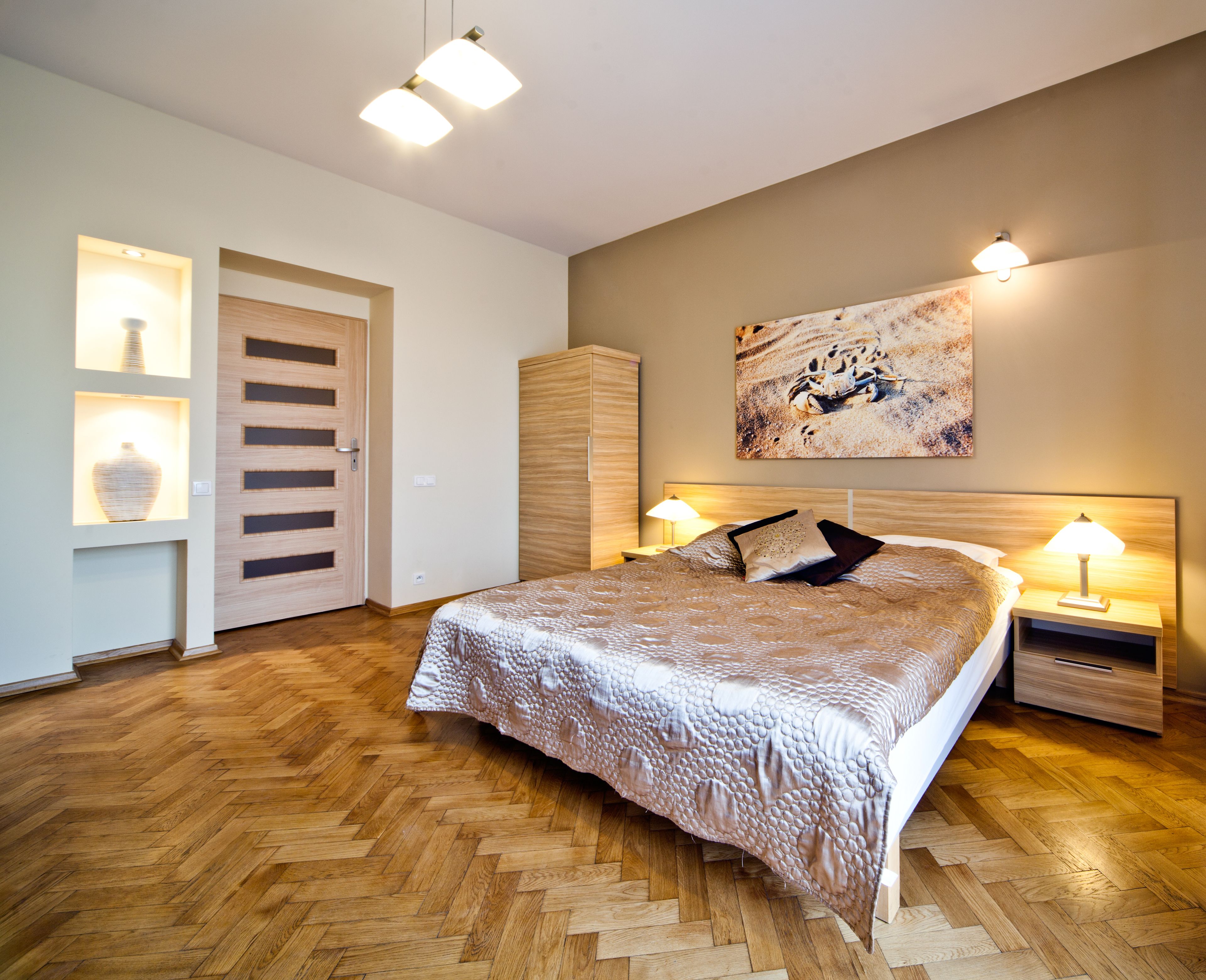 Ein Schlafzimmer mit einem großen Bett, Holzboden, einem Kleiderschrank, einem Nachttisch mit Lampe und einem an der Wand hängenden Kunstwerk.