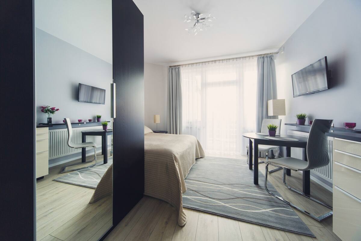 A modern hotel room with a bed, desk, chair, and a flat-screen TV.