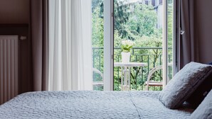 Un dormitorio con un ventanal grande, una cama blanca y vistas a un balcón con vegetación.