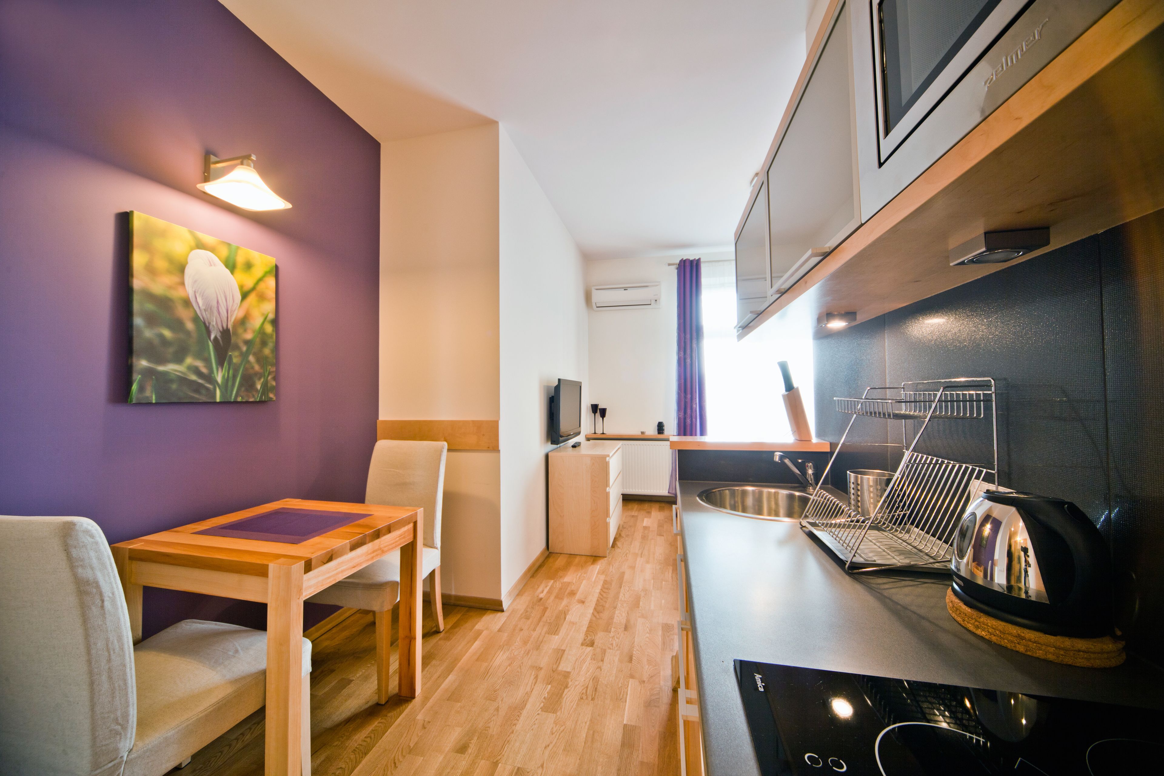 A compact kitchen with a wooden table and chairs, a microwave, and a kettle on the counter.