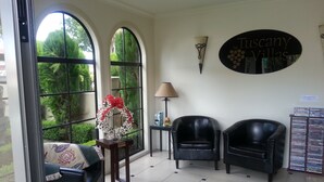 A room with a large window, a wreath on a table, two leather chairs, and a wall sign reading "Tuscany Villas". - Tuscany Villas Rotorua (Rotorua)