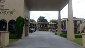 A building entrance with a covered walkway, parked cars, and a sign reading "UTIQUE COLLECTION." - Tuscany Villas Rotorua (Rotorua)