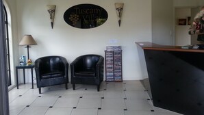 A reception area with a black leather sofa, a small table with a lamp, and a wall-mounted sign reading "Tuscany Villas". - Tuscany Villas Rotorua (Rotorua)