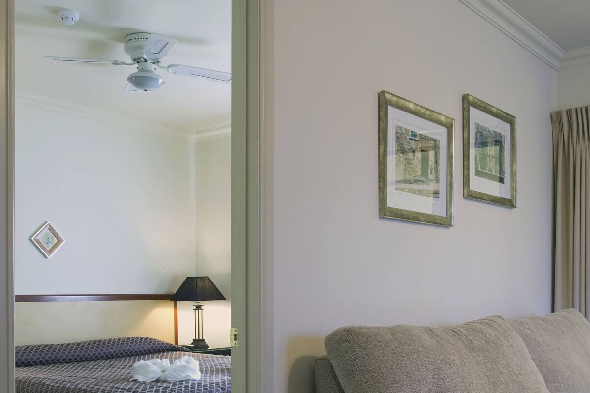 A hotel room with a bed, a sofa, a ceiling fan, and two framed pictures on the wall.