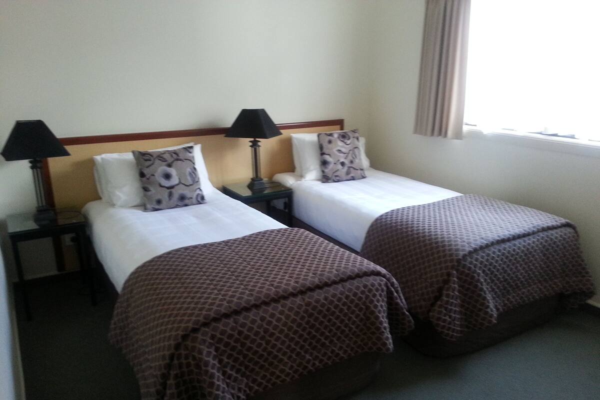A hotel room with two single beds, each with a pillow and a lamp.
