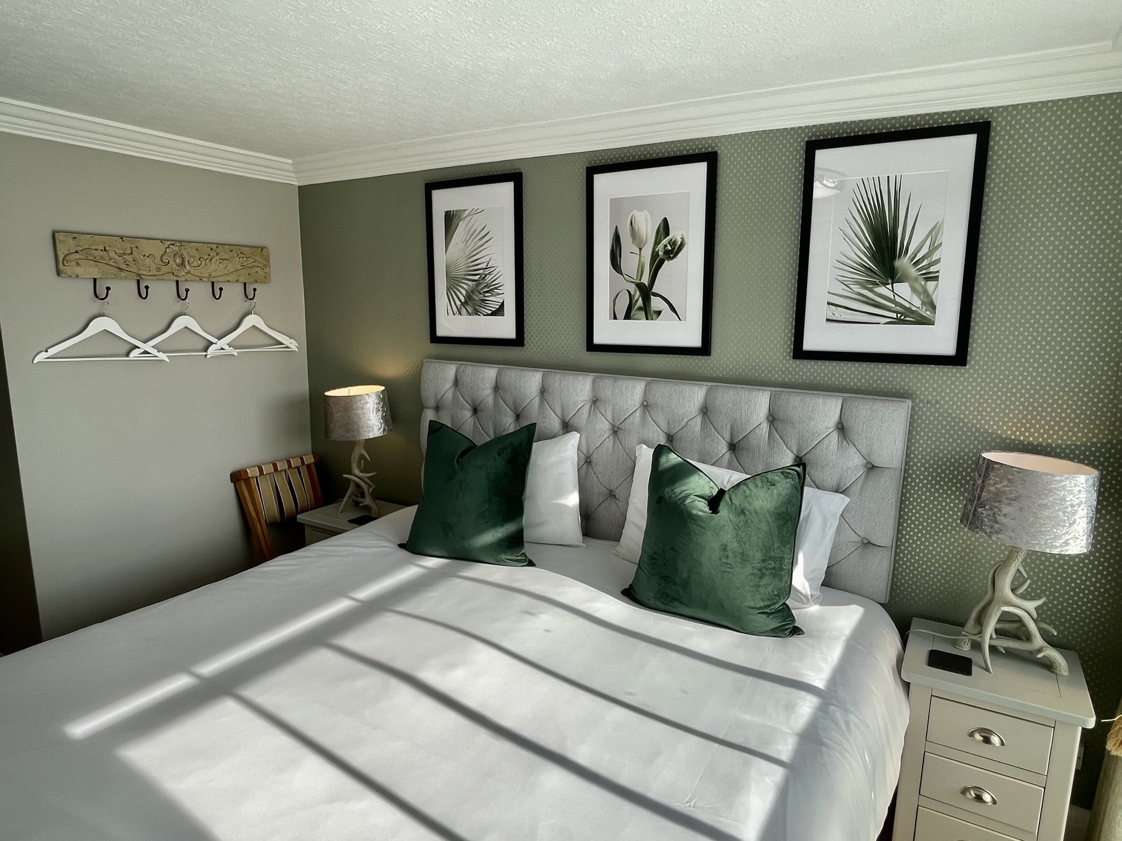 Un dormitorio ordenado con una cama grande, una mesita de noche, una lámpara e impresiones botánicas enmarcadas en la pared.