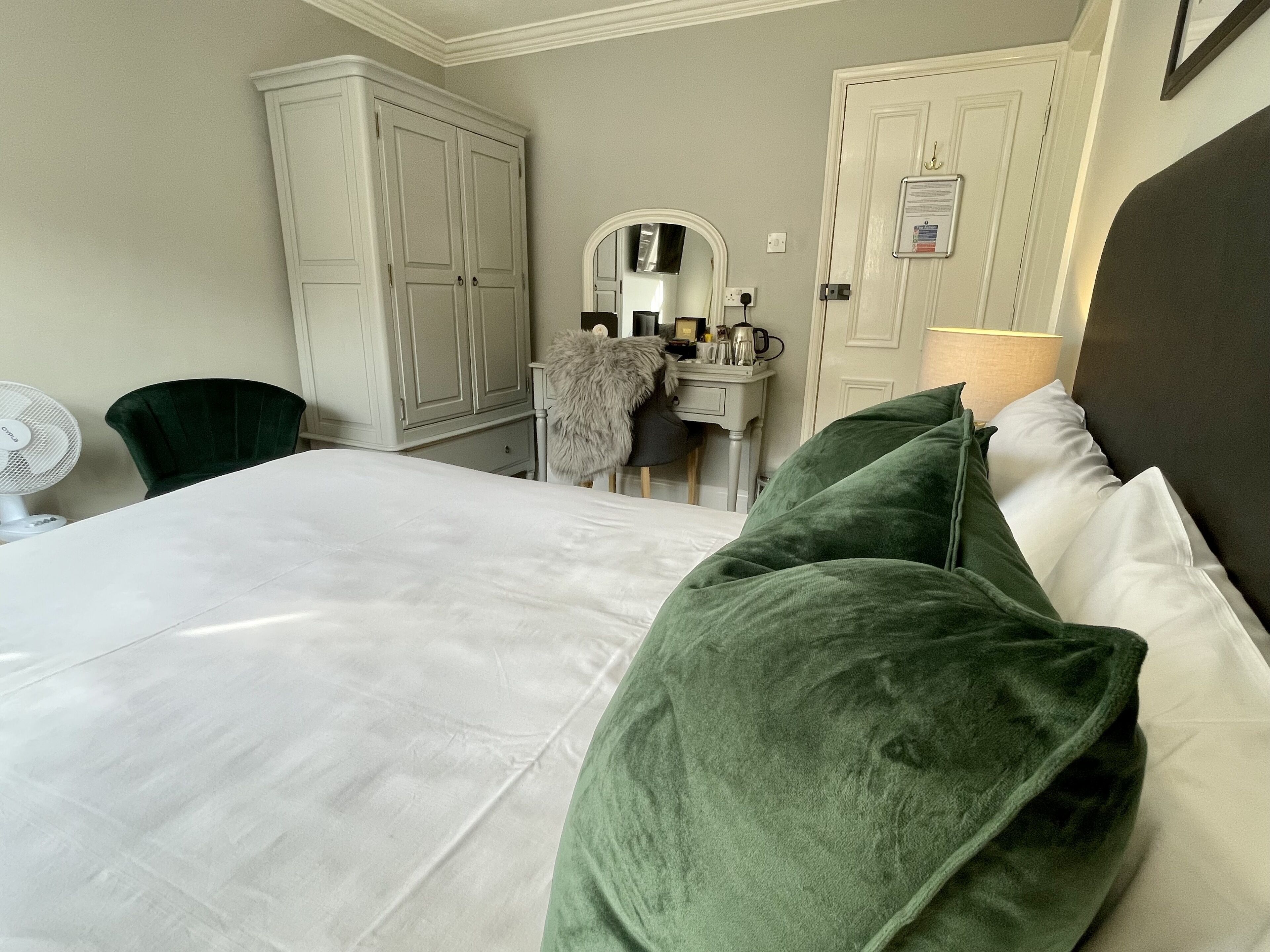A hotel room with a bed, a desk, a chair, a mirror, and a wardrobe.