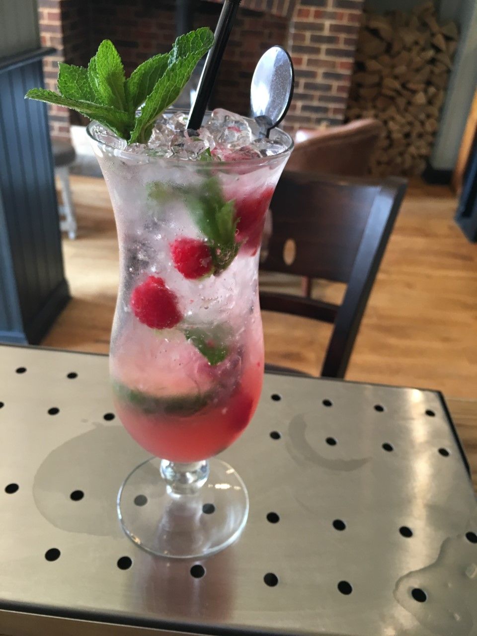 Un cocktail con ghiaccio, menta e lamponi in un bicchiere su un tavolo di metallo.