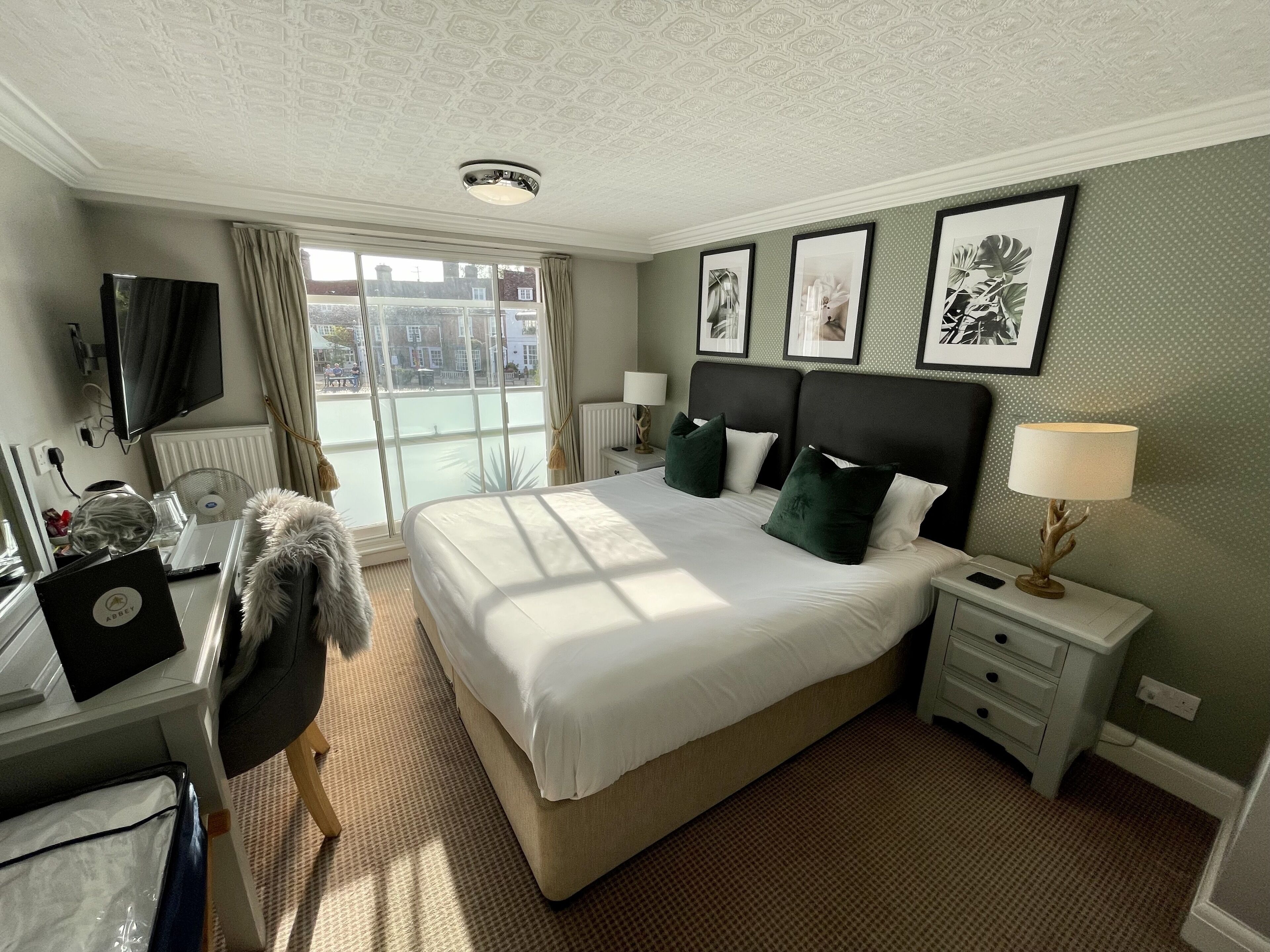 A hotel room with a large bed, a desk with a laptop, a TV, and a view of the city through the window.