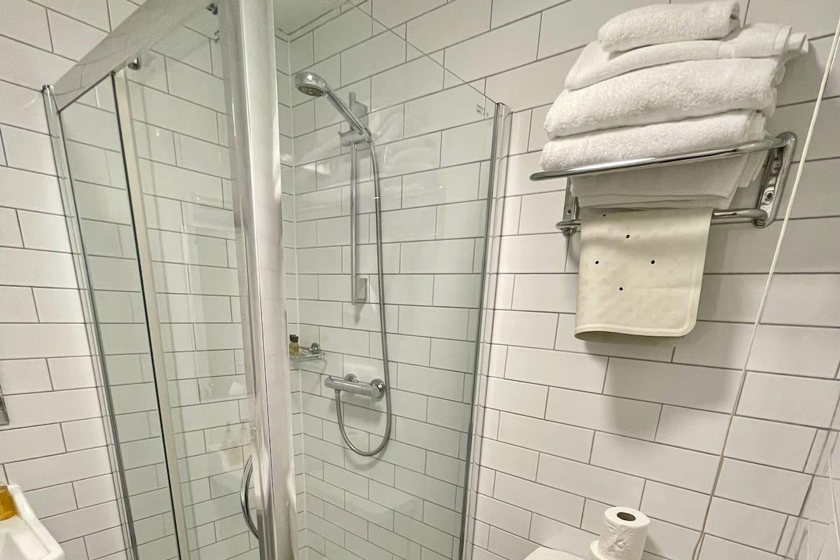 A bathroom with a glass-enclosed shower, a wooden toilet seat, and a white sink.